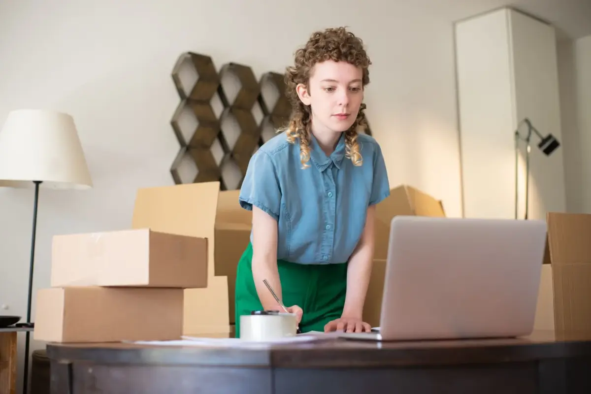 Home-based business owner packing orders beside stacked boxes